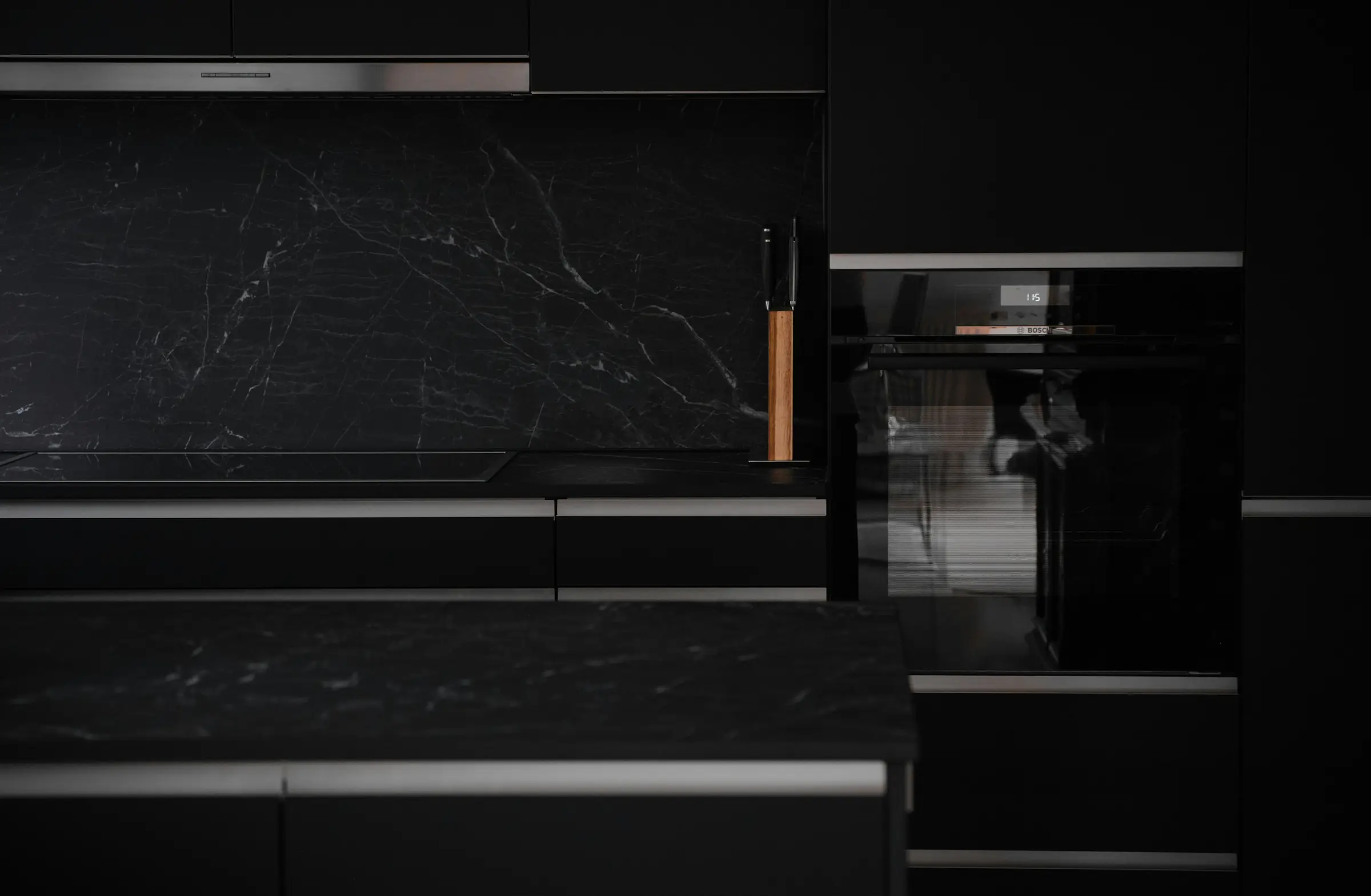 A matte-black kitchen with a built-in oven and a dark marble splashback